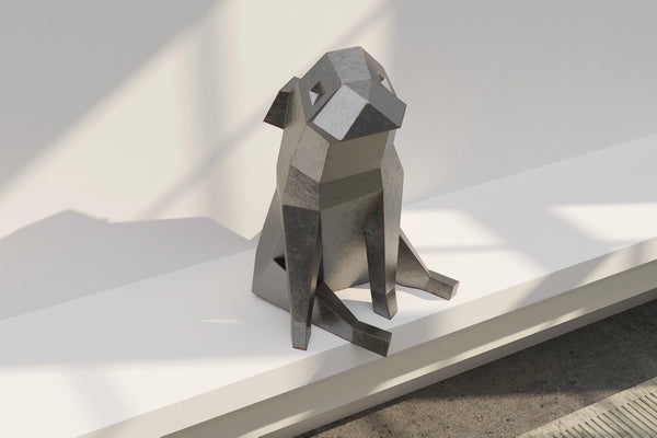 Sculpture de chien stylisée en métal gris sur un rebord blanc.