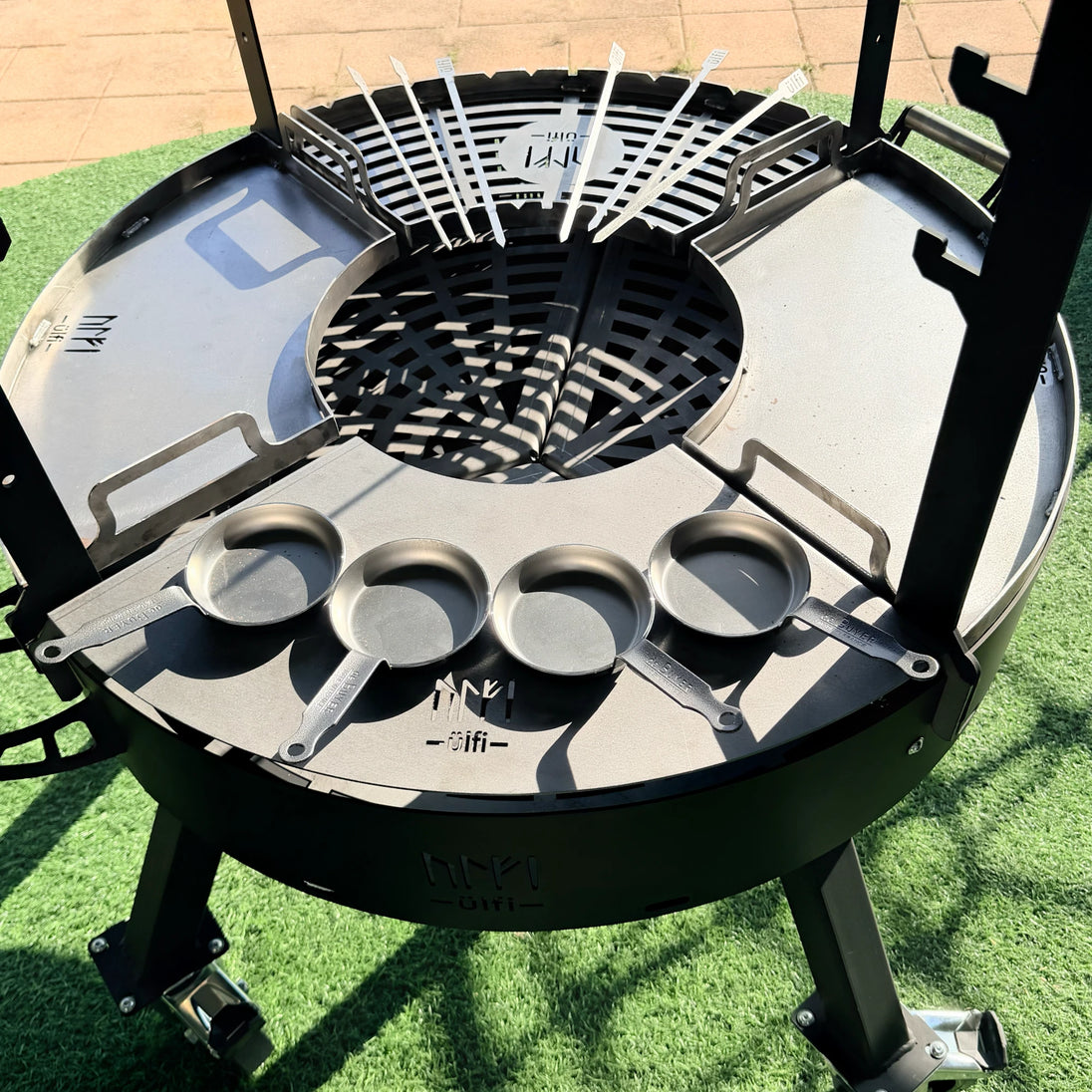 Barbecue circulaire en métal avec poêles de cuisson et grille de cuisson sur pieds.