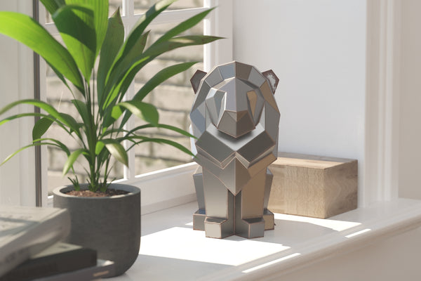 Sculpture géométrique en métal d'un lion sur un rebord de fenêtre avec une plante verte.
