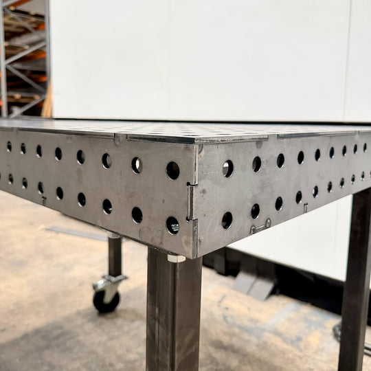 Table de soudure sur mesure en métal avec plateau perforé et pieds sur roulettes.